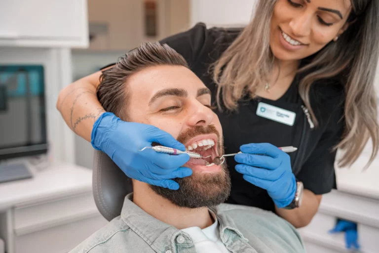 Man getting his teeth checked in a chair by a dental hygienist.