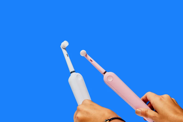 Photo of a white and a pink electric toothbrush on a blue background.