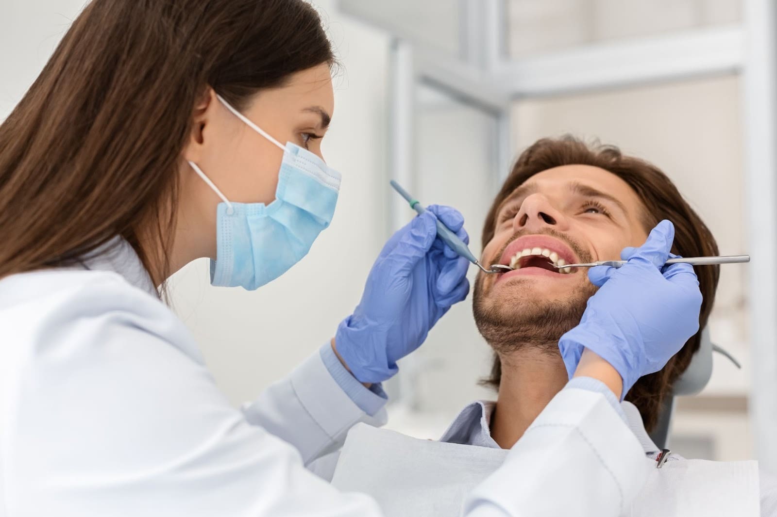 Female dental hygienist performing a comprehensive intra-oral and extra-oral screening and dental and periodontal exam on a male patient in the chair.