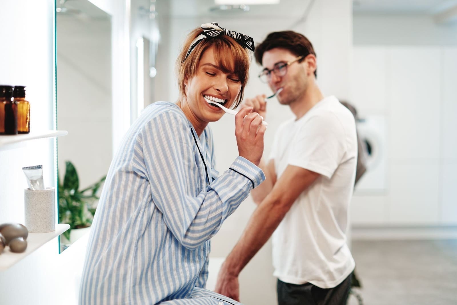 Couple in pajamas brushing their teeth together, demonstrating positive daily dental hygiene services and promoting family dental services.