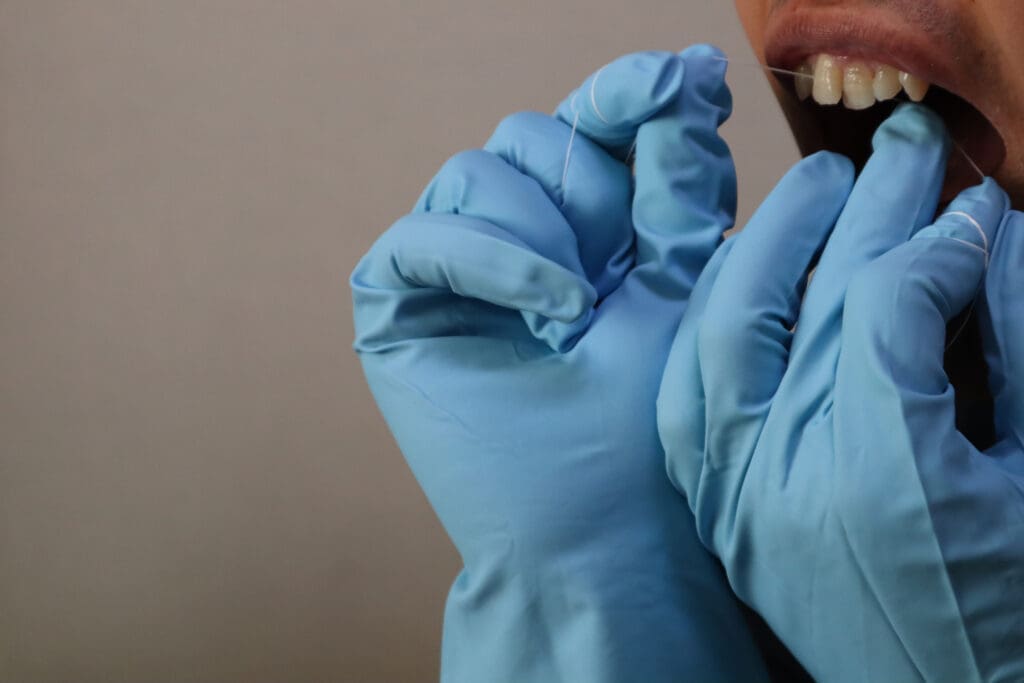 Close-up of a patient receiving professional dental care, showing a dental hygienist's gloved hands (wearing blue nitrile gloves) operating an ultrasonic scaler tool on the patient's molar. The equipment is used for a deep cleaning, scaling, and tartar removal procedure. Illustrates modern preventative dentistry and routine hygiene appointments.