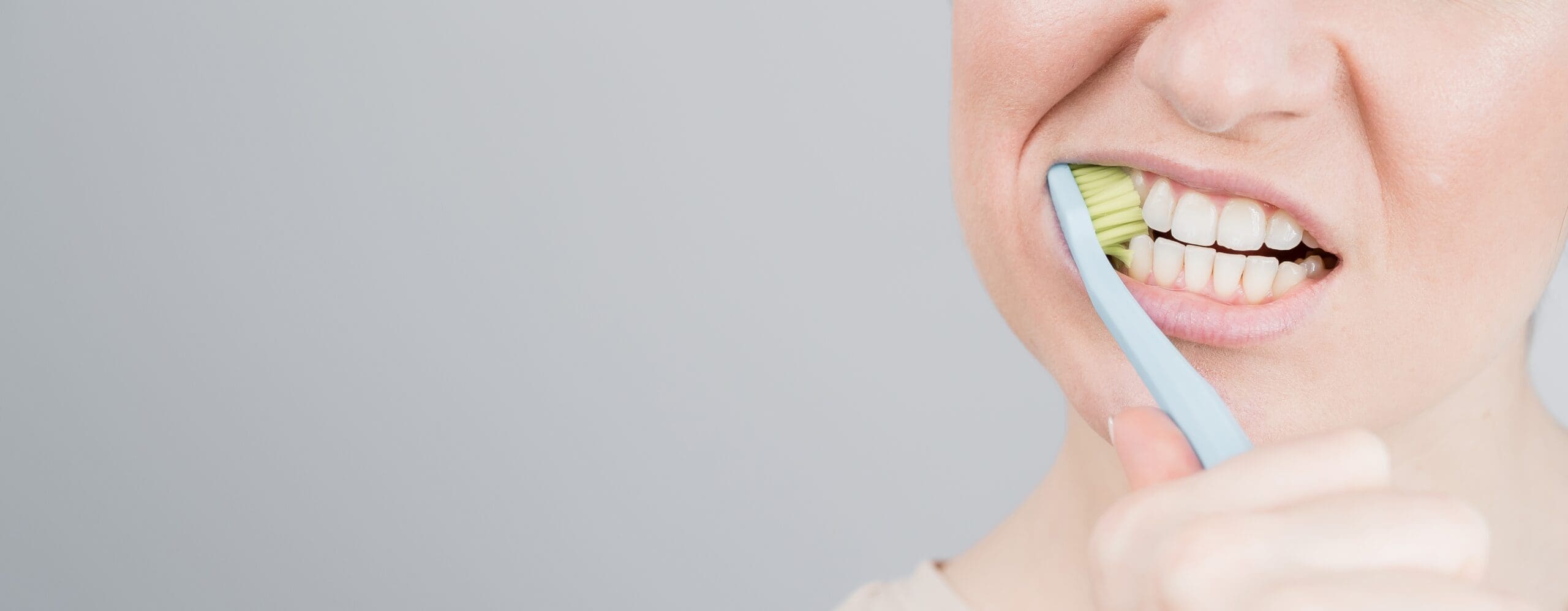 Close-up of a patient receiving professional dental care, showing a dental hygienist's gloved hands (in blue nitrile gloves) operating an ultrasonic scaler tool on the patient's molar. The equipment is used for a deep cleaning, scaling, and tartar removal procedure. Illustrates modern preventative dentistry and routine hygiene appointments.